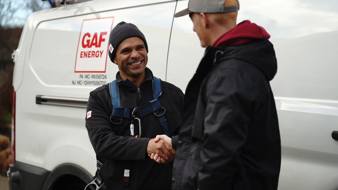 Nery in a harness beside a GAF Energy van, shaking hands with a contractor